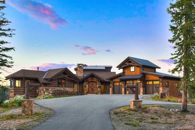 view of front of home featuring aphalt driveway, stone siding, and a chimney