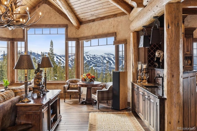 sunroom featuring vaulted ceiling with beams, wooden ceiling, an inviting chandelier, a mountain view, and a sink