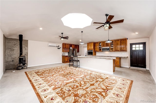 24130 High Timber Ln, Agate, CO 80101 - kitchen with a ceiling fan, brown cabinetry, appliances with stainless steel finishes, a wood stove, and a kitchen island with sink