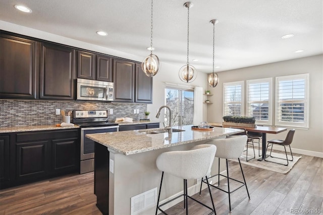 kitchen featuring pendant lighting, sink, stainless steel appliances, and a kitchen island with sink