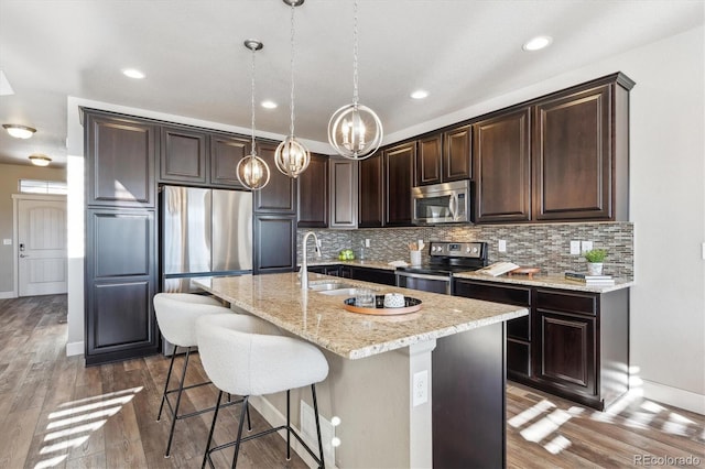 kitchen featuring dark brown cabinets, stainless steel appliances, dark wood-type flooring, decorative light fixtures, and a center island with sink