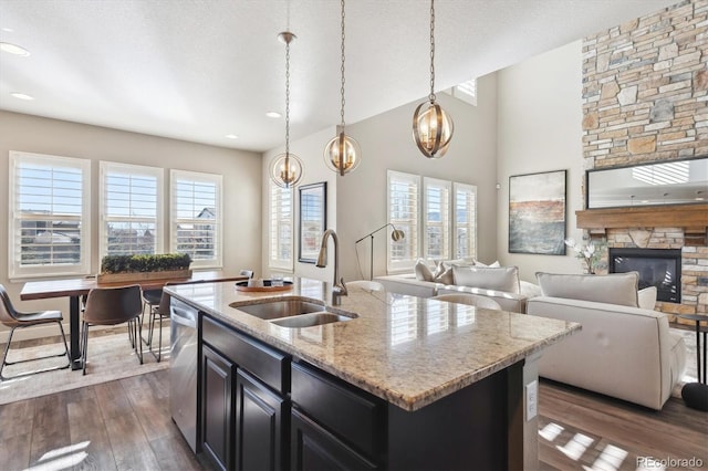 kitchen with pendant lighting, sink, light stone countertops, a fireplace, and an island with sink