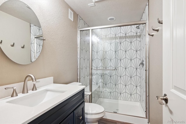 bathroom with vanity, toilet, a shower with door, and a textured ceiling