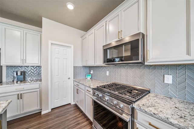 kitchen with decorative backsplash, dark wood-style flooring, appliances with stainless steel finishes, light stone countertops, and white cabinetry