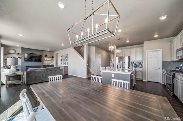 dining room with a large fireplace, stairway, dark wood-style floors, a chandelier, and recessed lighting