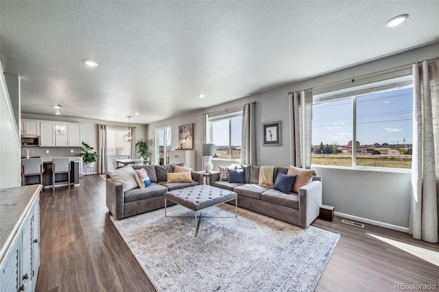 living area featuring dark wood-style flooring, a textured ceiling, visible vents, baseboards, and recessed lighting
