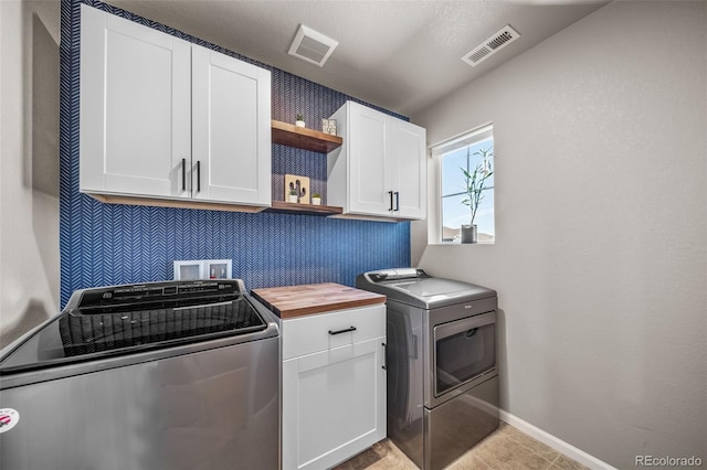 washroom with baseboards, washing machine and dryer, visible vents, and cabinet space