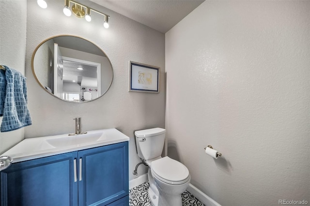 half bath featuring vanity, baseboards, tile patterned floors, and toilet