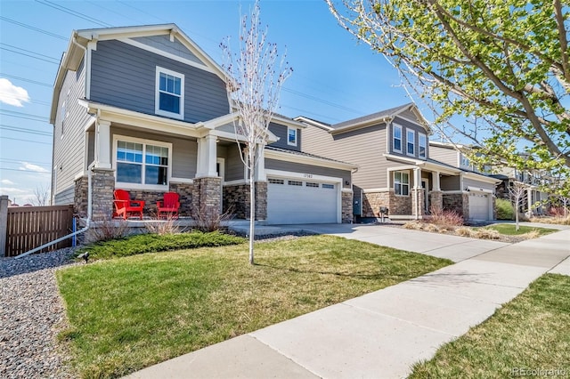 craftsman house with covered porch, concrete driveway, a front yard, and stone siding