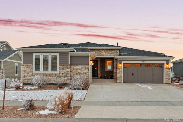 prairie-style house featuring driveway, stone siding, and a garage