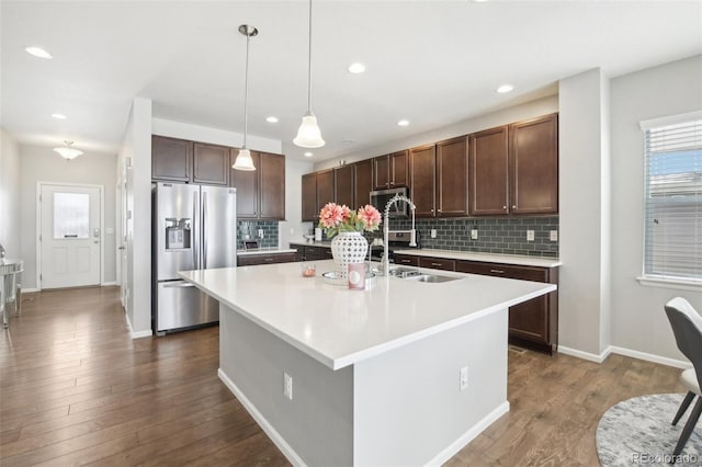 kitchen featuring dark wood-type flooring, appliances with stainless steel finishes, a kitchen island with sink, hanging light fixtures, and tasteful backsplash