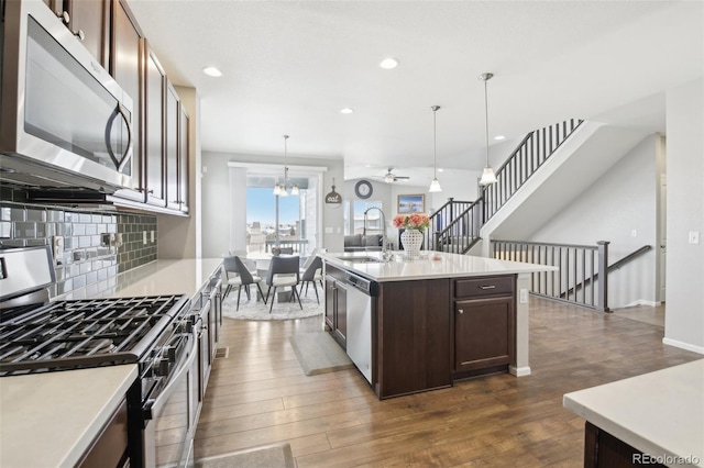 kitchen with sink, hanging light fixtures, stainless steel appliances, dark wood-type flooring, and a center island with sink