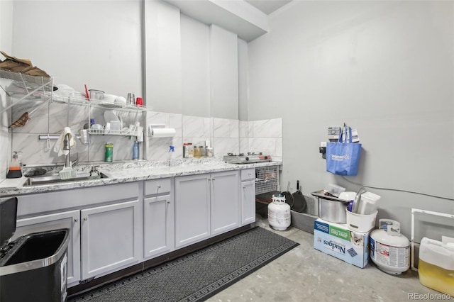 interior space featuring tasteful backsplash, light stone countertops, sink, and white cabinets