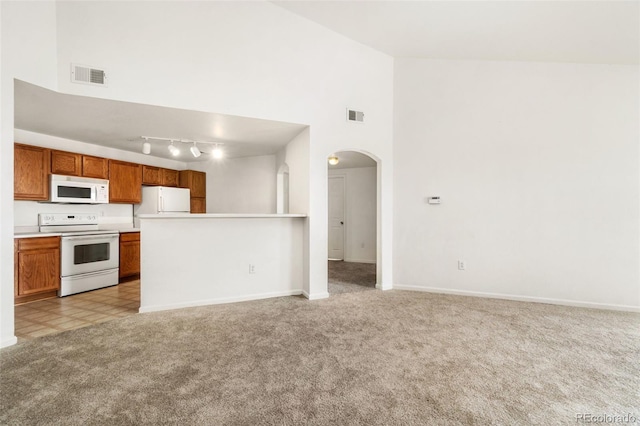 kitchen with high vaulted ceiling, white appliances, track lighting, and light colored carpet