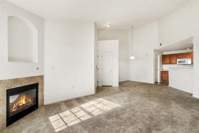 unfurnished living room featuring a tile fireplace, light carpet, and high vaulted ceiling