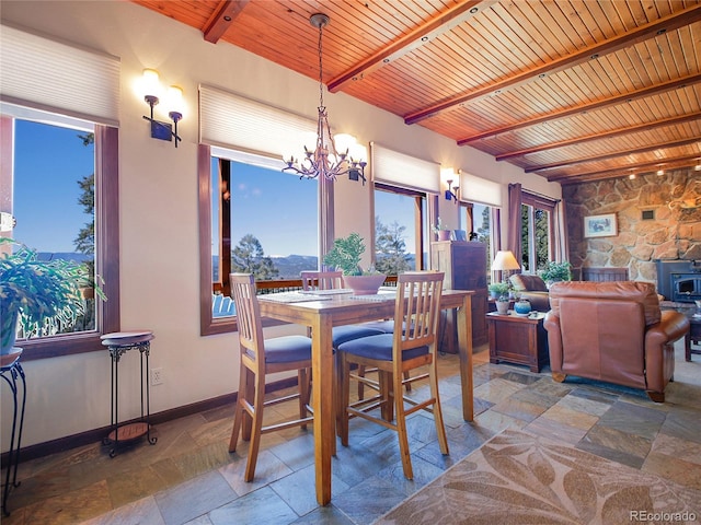 13012 S Wamblee Valley Rd, Conifer, CO 80433 - dining room featuring stone tile floors, a chandelier, wooden ceiling with exposed beams, a wood stove, and baseboards