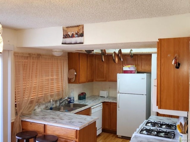 kitchen featuring kitchen peninsula, sink, white appliances, light wood-type flooring, and a textured ceiling