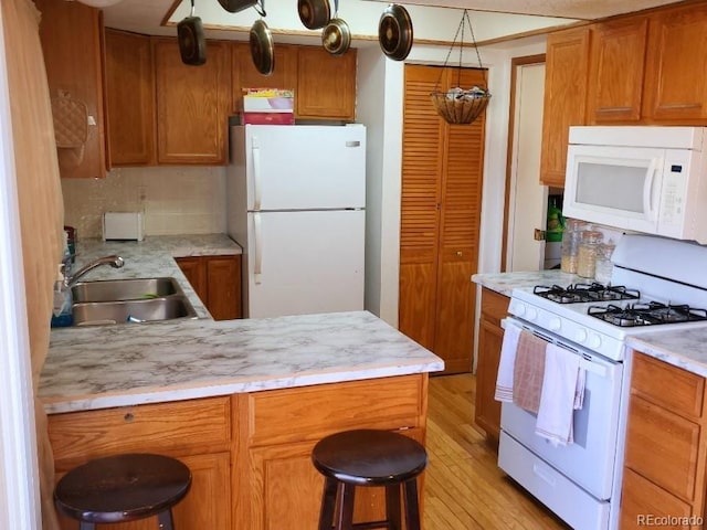 kitchen with white appliances, light hardwood / wood-style floors, sink, backsplash, and a breakfast bar