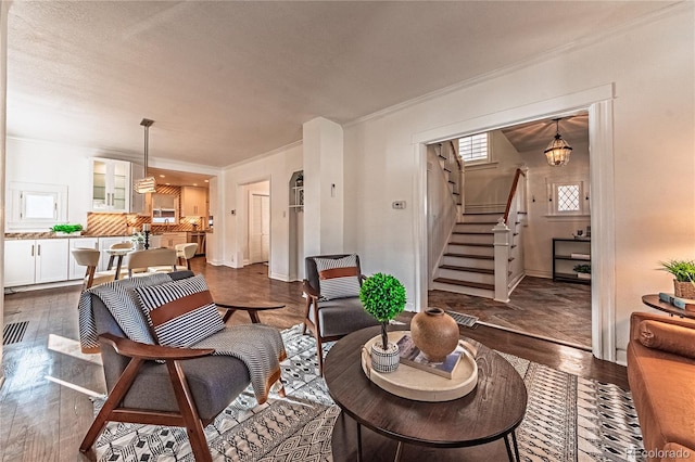 living area with stairs, dark wood-type flooring, a notable chandelier, and ornamental molding