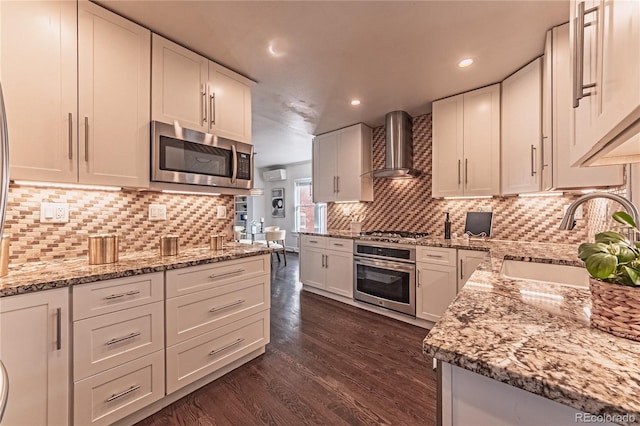 kitchen with a sink, dark wood-type flooring, appliances with stainless steel finishes, white cabinetry, and wall chimney exhaust hood