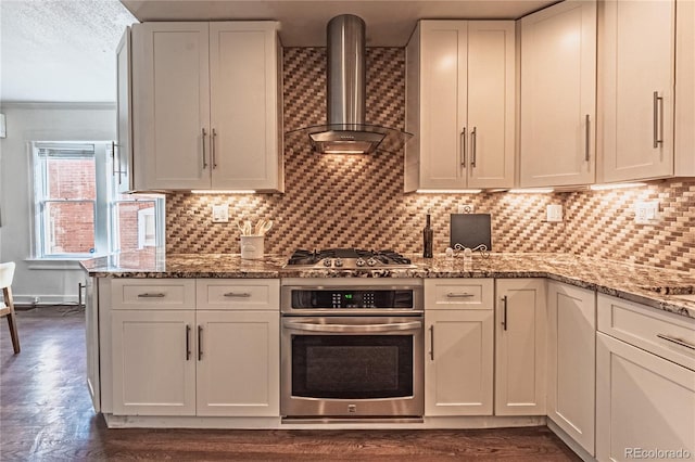 kitchen featuring tasteful backsplash, white cabinetry, stainless steel appliances, and wall chimney exhaust hood