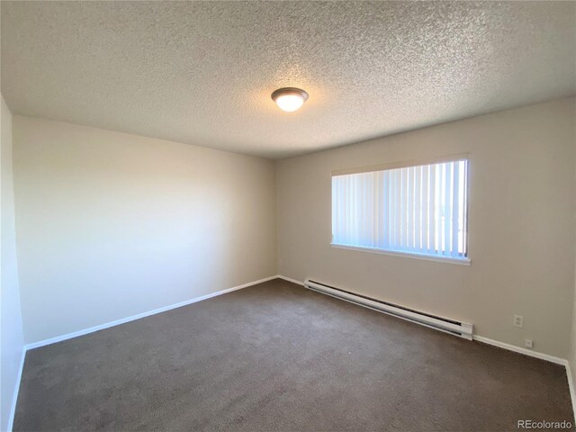 spare room with dark carpet, a textured ceiling, and a baseboard heating unit