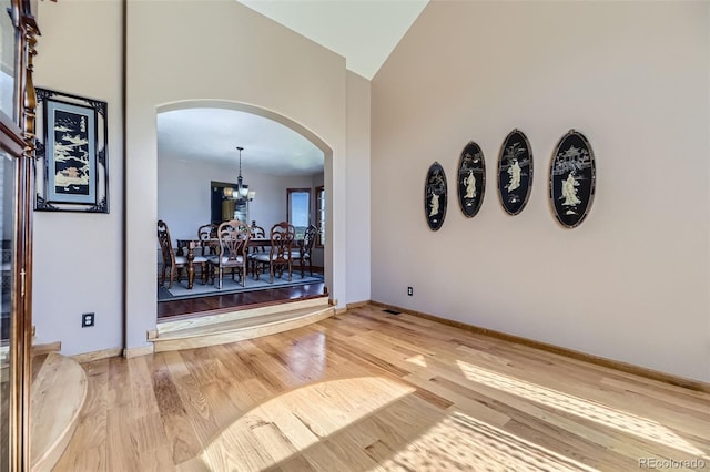 7043 S Owens Way, Littleton, CO 80127 - empty room featuring arched walkways, high vaulted ceiling, a chandelier, and light wood finished floors