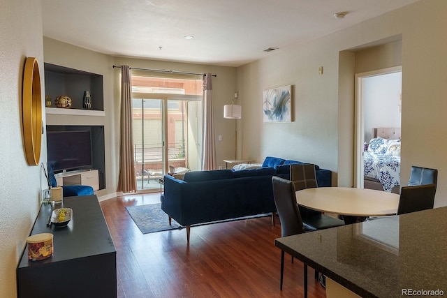 living room with a fireplace, built in features, and dark wood-type flooring