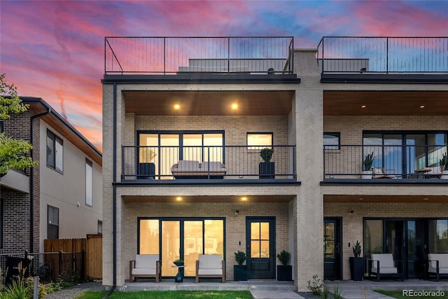 1645 N Osceola St, Denver, CO 80204 - back of property at dusk featuring a balcony, brick siding, and a patio
