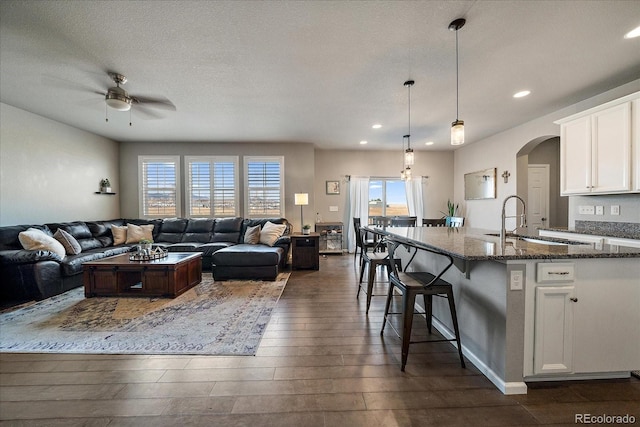 living room with a textured ceiling, ceiling fan, sink, and dark wood-type flooring