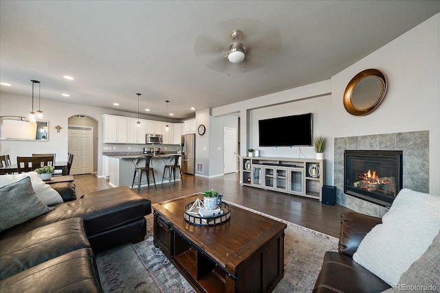 living room with a tile fireplace, ceiling fan, and wood-type flooring