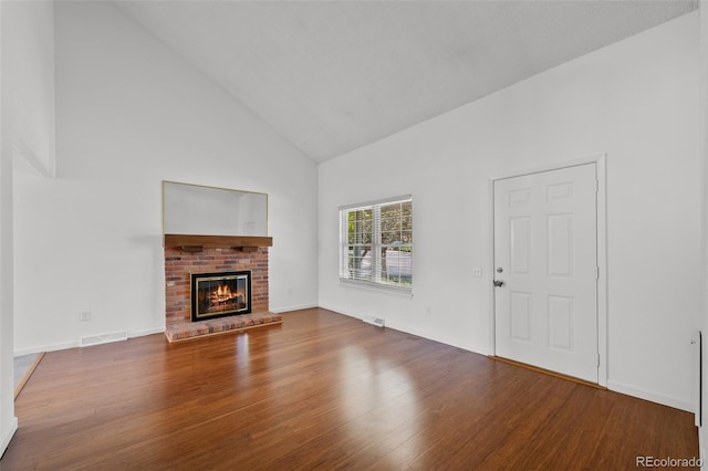 unfurnished living room featuring visible vents, a brick fireplace, wood finished floors, and high vaulted ceiling