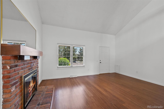 unfurnished living room with wood-type flooring, visible vents, a brick fireplace, baseboards, and vaulted ceiling