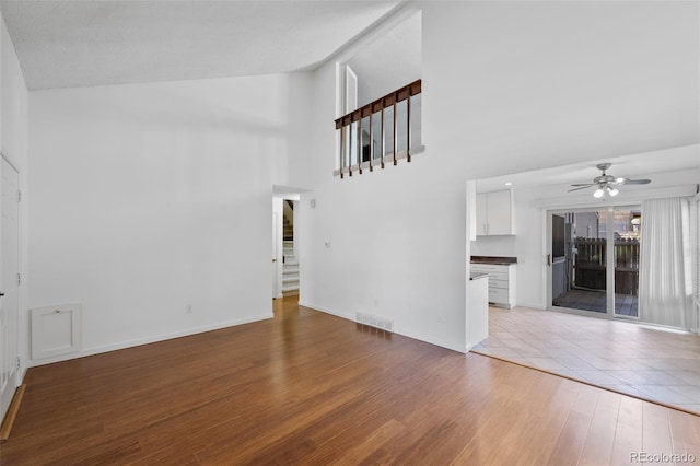 unfurnished living room featuring visible vents, high vaulted ceiling, stairway, a ceiling fan, and light wood finished floors
