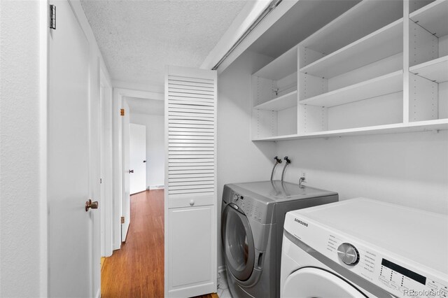 clothes washing area with light wood-style floors, laundry area, a textured ceiling, and washer and clothes dryer