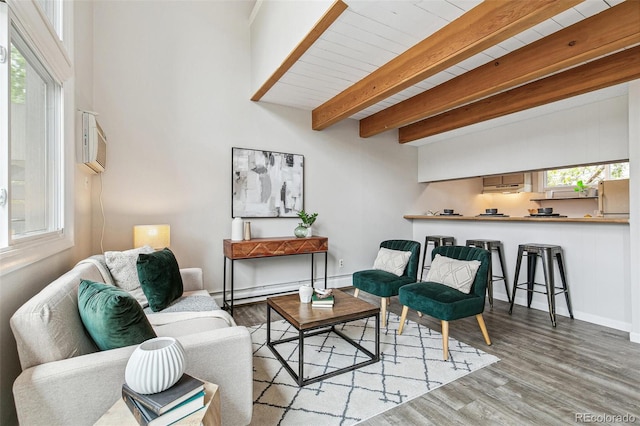 living area with a wall unit AC, wood finished floors, a healthy amount of sunlight, and beamed ceiling