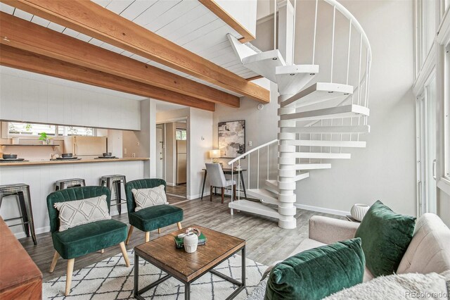 living area with baseboards, beamed ceiling, wood finished floors, and stairway
