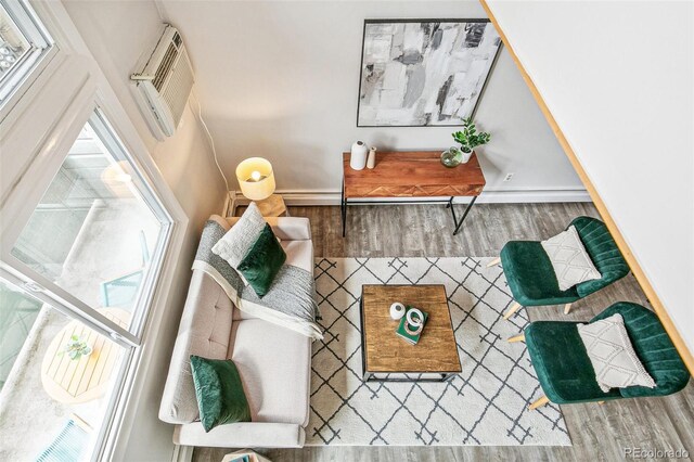 living area featuring an AC wall unit, baseboards, a healthy amount of sunlight, and wood finished floors
