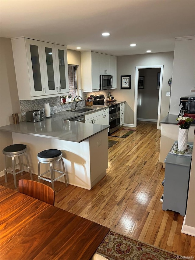 kitchen featuring kitchen peninsula, stainless steel appliances, a kitchen bar, and white cabinetry