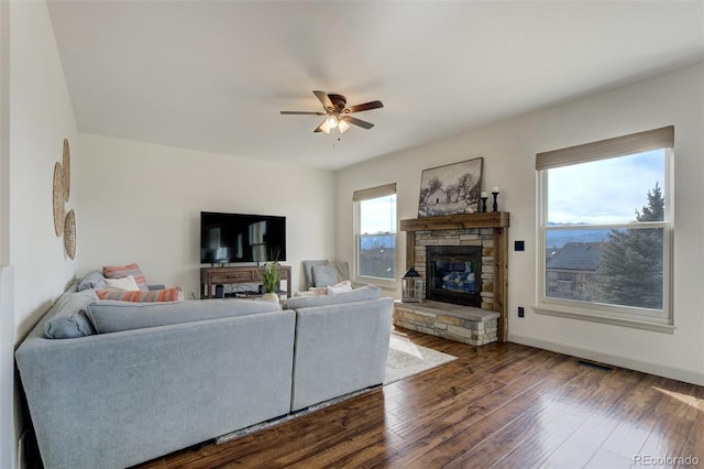 living room with a ceiling fan, visible vents, baseboards, a fireplace, and dark wood-type flooring