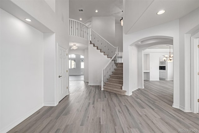 foyer entrance with stairs, arched walkways, baseboards, and wood finished floors