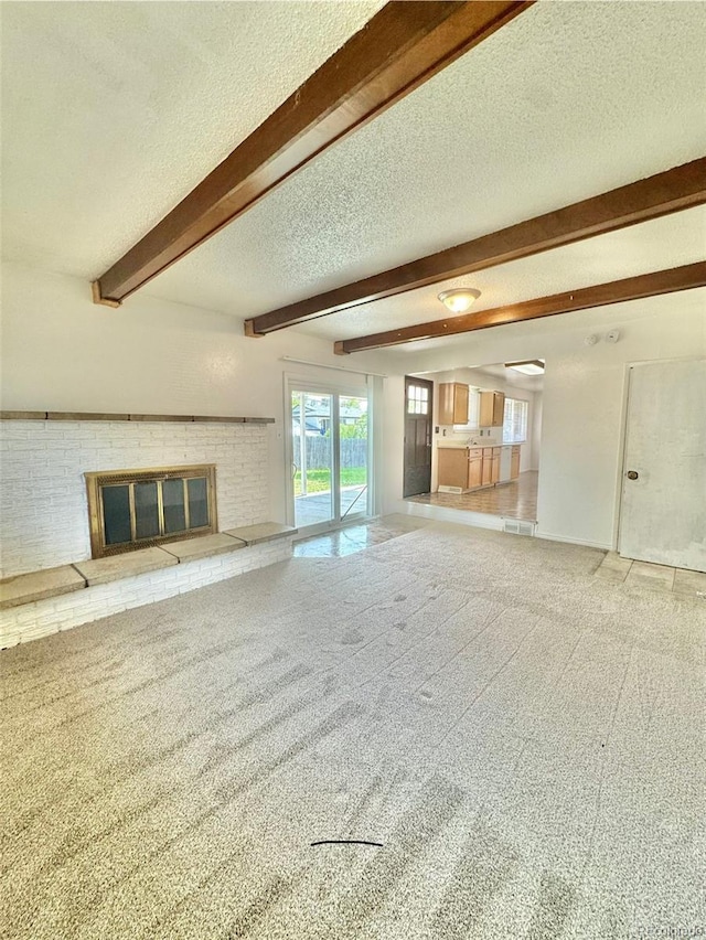 13024 E Alaska Pl, Aurora, CO 80012 - unfurnished living room with a textured ceiling, beam ceiling, a brick fireplace, and carpet floors
