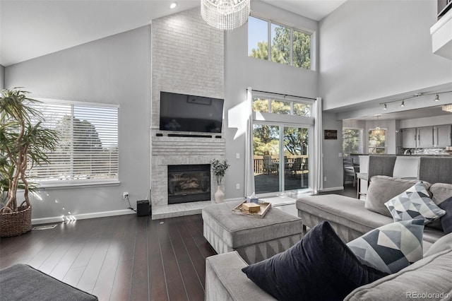 living room featuring baseboards, wood finished floors, an inviting chandelier, a fireplace, and high vaulted ceiling