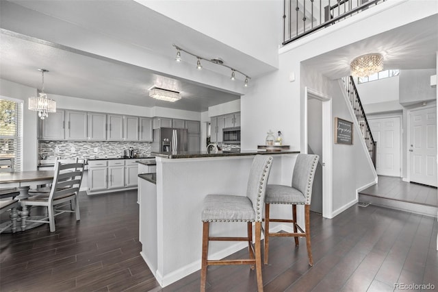 kitchen featuring gray cabinetry, a notable chandelier, dark wood-style flooring, appliances with stainless steel finishes, and dark countertops