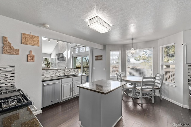 kitchen featuring dark wood finished floors, a kitchen island, backsplash, stainless steel dishwasher, and a sink