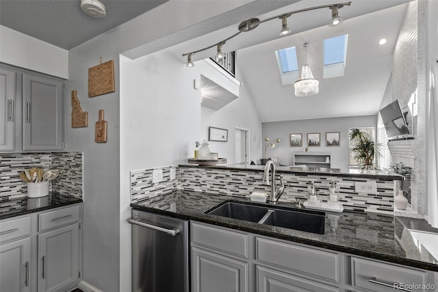 kitchen featuring decorative backsplash, lofted ceiling with skylight, dark stone countertops, a sink, and stainless steel dishwasher