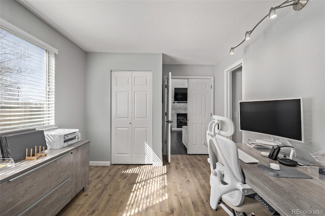 home office featuring light wood-type flooring, a fireplace, and baseboards