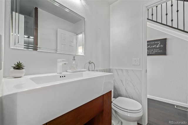 bathroom featuring tile walls, toilet, wainscoting, vanity, and wood finished floors