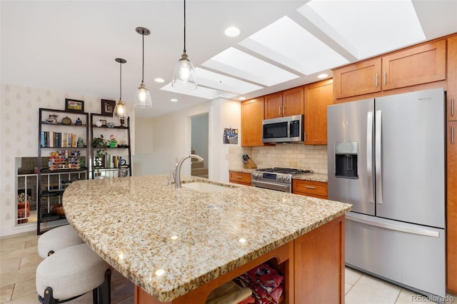 kitchen with sink, a center island with sink, light stone counters, and appliances with stainless steel finishes