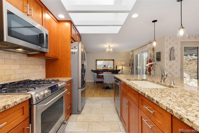 kitchen with sink, decorative light fixtures, light stone counters, a skylight, and appliances with stainless steel finishes